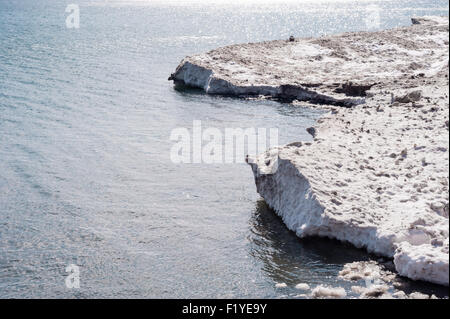 Flanke von schmutzigen weißen und braunen Eisschollen und Schnee am Wasser tagsüber, mit teilweise geschmolzenem Eis in Wasser. Stockfoto