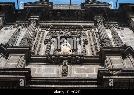 MEXIKO-STADT, Mexiko – verzierte Kolonialsteinmauerwerke und eine religiöse Statue zieren die Fassade über dem Eingang zur Iglesia de San Bernardino. Die Kirche aus dem 17. Jahrhundert zeigt die aufwendige architektonische Dekoration, die typisch für den mexikanischen Barockstil ist. In diesem historischen Gebäude in der Nähe von Zocalo in Mexiko-Stadt sind die ursprünglichen Elemente der Kolonialfassade erhalten geblieben. Die skulpturalen Details zeigen die raffinierten Steinschnitzertraditionen der religiösen Kolonialarchitektur. Stockfoto