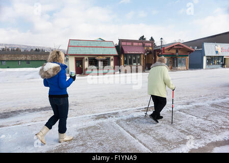 Zwei kaukasischen Frau tragen Mäntel und Stiefel zu Fuß auf dem Gehweg vorbei an Geschäften in der Stadt während des Winters, Grand Marais, MN, USA Stockfoto