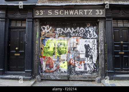 33 bis 35 Fournier Street, Spitalfields, London. Georgische Handwerker Doppeltür Hof Eingang flankiert von zwei typischen historischen Haustüren mit rechteckigen Oberlichtern. SignWriting über dem Eingang sagt '33A S. SCHWARTZ'. Graffiti und Plakate an den Türen. Stockfoto