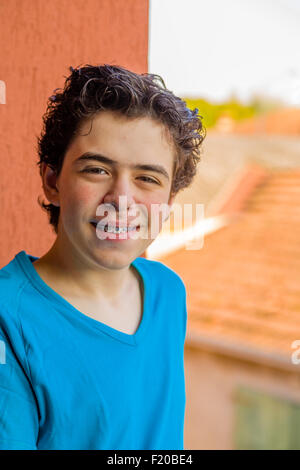 Lateinische junge lächelt Klammern zeigen, während er einen Tablet-PC mit einem roten Grunge Wand- und Dorf Dächer als Hintergrund hält Stockfoto