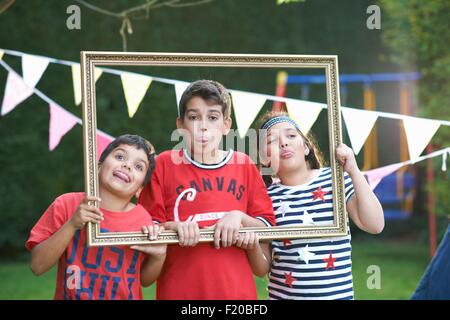 Drei Kinder durchsehen Bilderrahmen, Zungen herausragen Stockfoto