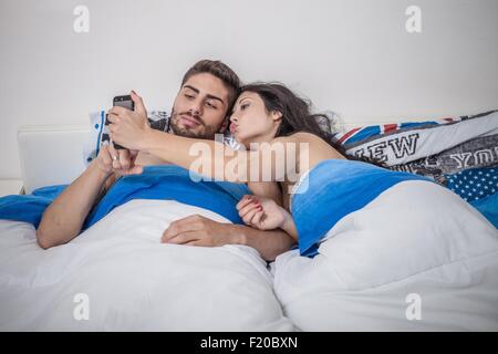 Junges Paar unter Smartphone Selfie im Bett Stockfoto