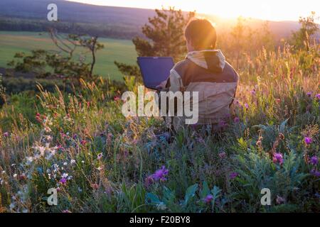 Mitte erwachsenen Mann sitzt in Wildblumenwiese mit laptop Stockfoto