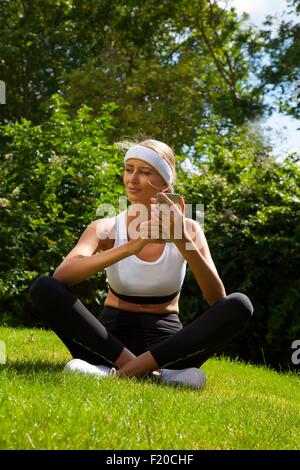 Frau trägt Sportshirt mit Smartphone im Garten Stockfoto