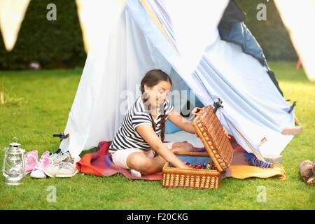 Mädchen, die Entleerung der Picknick-Korb vor hausgemachten Zelt im Garten Stockfoto