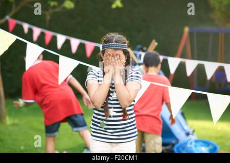 Mädchen über ihr Augen für Hide and seek mit Brüder im Garten Stockfoto