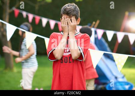 Junge für seine Augen für hide and seek mit Schwester und Bruder im Garten Stockfoto