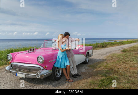 Junges Paar Blick auf Karte neben Oldtimer Cabrio an Küste, Havanna, Kuba Stockfoto