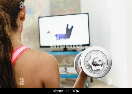 Junge Frau, die das Training mit Hanteln im Wohnzimmer während Computer-Bildschirm anschauen Stockfoto