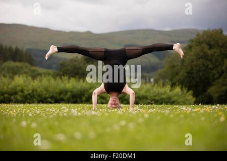 Reife Frau praktizieren Yoga auf Kopf mit Beinen stehend im Feld öffnen Stockfoto