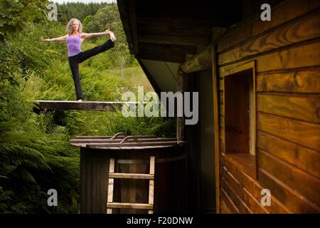 Reife Frau praktizieren Yoga-Pose auf Steg in Eco lodge Stockfoto