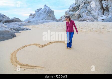 Mitte Erwachsene Frau am Strand, Zeichnung Herzform mit Füßen Stockfoto