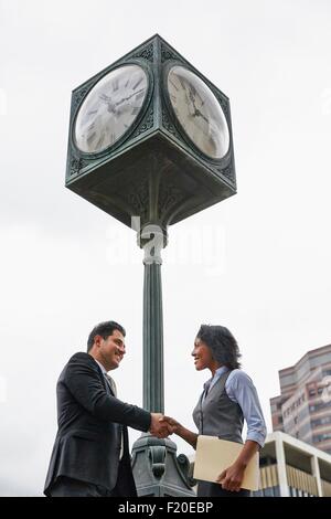 Niedrigen Winkel Ansicht Seitenansicht der Geschäftsleute Händeschütteln unter Uhr, Hüfte aufwärts Stockfoto