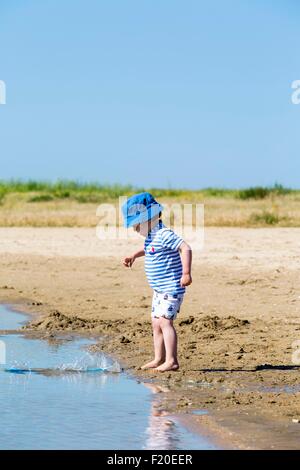 Kleiner Junge am Strand werfen Sand ins Meer, Marennes, Charente-Maritime, Frankreich Stockfoto