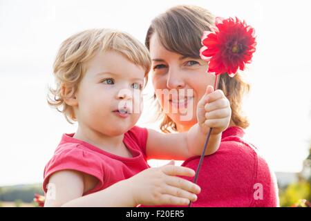 Porträt von Mitte Erwachsene Mutter und Kleinkind Tochter halten rote Blume im Feld Stockfoto