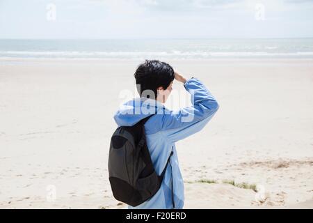 Mitte Erwachsene Frau am Strand Abschirmung Augen und Blick auf das Meer Stockfoto