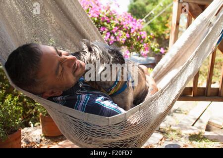Mitte erwachsener Mann im Garten Hängematte mit Hund Stockfoto