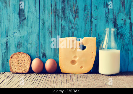 ein Toast, einigen Eiern, ein Stück Schweizer Käse und eine Flasche mit Milch auf einem rustikalen Holztisch, gegen einen blauen rustikalen hölzernen backgr Stockfoto