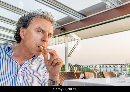 Magische Momente zu teilen, wie ein ruhiges Abendessen im Restaurant mit Blick aufs Meer bei Sonnenuntergang: lustige Mann mittleren Alters isst Pommes frites Stick Stockfoto