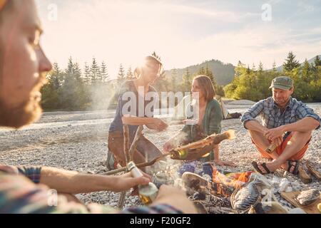 Erwachsene sitzen um Lagerfeuer Kochen Fisch Stockfoto