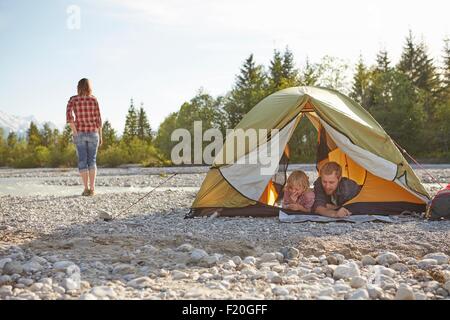 Familie auf Fronten im entpackten Zelt, nebeneinander liegend auf der Suche auf Karte Stockfoto