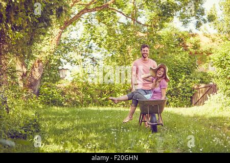 Junges Paar, Mann Frau in Schubkarre schieben, lachen Stockfoto