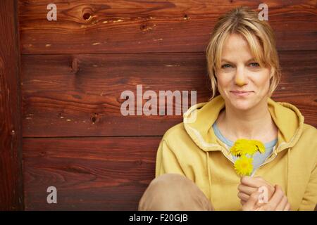 Reife Frau sitzen Holzhütte, Holding gelbe Blüten, gelbe Nase aus Blumen riechen Stockfoto