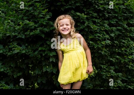 Porträt des Lächelns blonde kurzhaarige Mädchen tragen gelbe Kleid stand vor Garten Hecke Stockfoto