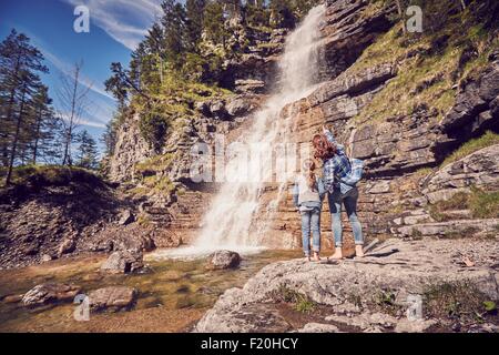 Mutter und Tochter stehen auf Felsen, Wasserfall, beobachtete Rückansicht Stockfoto