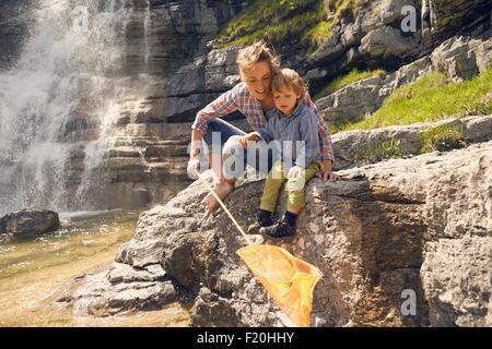 Mutter und Sohn, sitzen auf den Felsen von Wasserfall, Fischen mit Netz Stockfoto