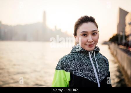 Porträt der jungen Frau trägt Trainingsjacke vor Wasser lächelnd Stockfoto