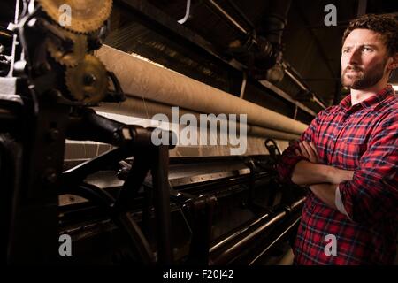 Porträt des jungen männlichen Weaver und alten Webmaschine in Textilfabrik