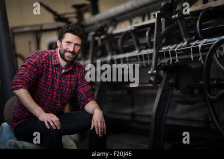 Porträt der jungen männlichen Weaver am alten Webmaschine in Textilfabrik
