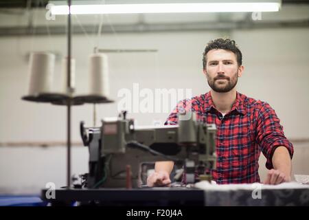 Porträt von männlichen Textildesignerin mit Nähmaschine in alten Textilfabrik Stockfoto