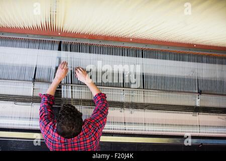 Draufsicht der junge männliche Weberin Anpassung Threads auf alten Webmaschine in Textilfabrik