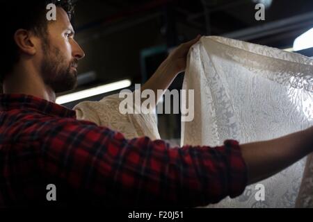 Porträt von männlichen Weaver Prüfung Spitzen Produkt aus alten Webmaschine in Textilfabrik Stockfoto