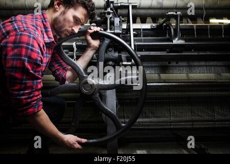 Männliche Weber Drehrad auf der alten Webmaschine in Textilfabrik Stockfoto