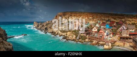 Malta, Mellieha, Anchor Bay, Panorama Überblick über das Dorf Popeye zur Aufnahme eines Spielfilms gebaut am Ufer unter einem bewölkten Himmel Stockfoto