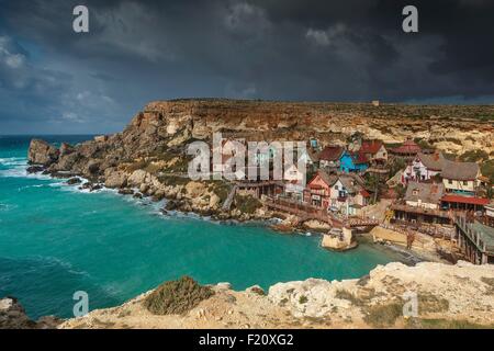 Malta, Mellieha, Anchor Bay, Panorama Überblick über das Dorf Popeye zur Aufnahme eines Spielfilms gebaut am Ufer unter einem bewölkten Himmel Stockfoto