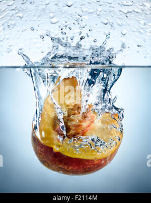 ein gelber Pfirsich große Erdbeer Tropfen im blauen Wasser mit Spritzern Stockfoto