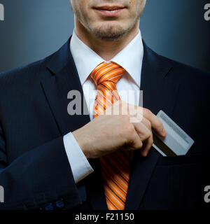 Kaufmann im schwarzen Kostüm und orange Krawatte setzen oder Kreditkarte in Tasche herausnehmen Stockfoto