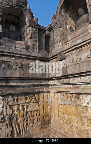 Indonesien, Java, Borobudur, Ecke einen Durchgang mit zwei benachbarten, sitzende Buddhas in Nischen und Stein Friese darunter. Stockfoto