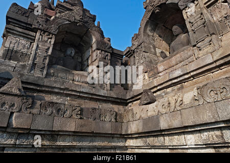 Indonesien, Java, Borobudur, zwei sitzende, Granit Buddhas im angrenzenden Ecke Nischen; eine mit einem gemalten weißen Gesicht. Stockfoto