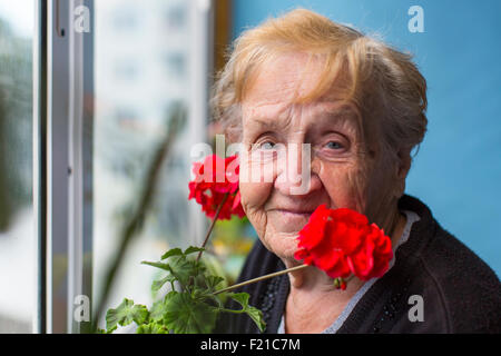 Porträt einer alten Frau auf dem Balkon mit roten Blüten. Stockfoto