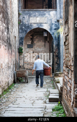 Reife Asiatin trägt einen Eimer kopfsteingepflasterten Gasse in Chengkan Dorf, China, Asien Stockfoto