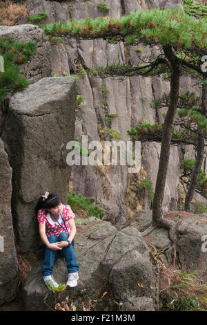 Mädchen in rosa Kaninchen oben sitzt auf einem Felsen entlang Helligkeit Peak Trail, gelben Berg Huangshan, Anhui Provinz, China, Asien Stockfoto