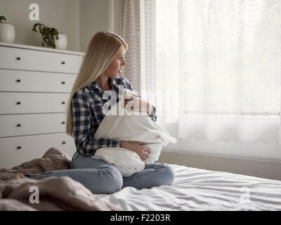 Nachdenkliche junge Frau sitzt auf dem Bett, traurige Gefühle Stockfoto