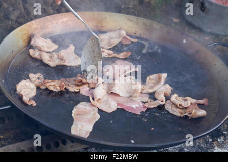 Speck braten in einer riesigen Pfanne auf eine externe Feuerstelle Stockfoto