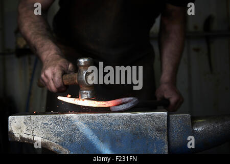 Ein Schmied, ein heißes Stück Eisen auf einem Amboss mit einem Hammer zu gestalten. Stockfoto